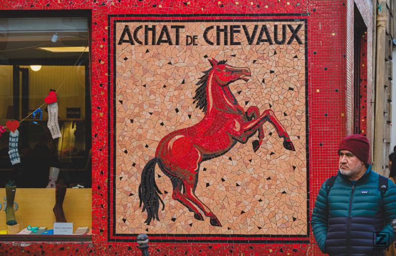 A tilled wall with a drawing of a horse and the title "Achat de Chevaux". Someone is standing on the right, not really happy. 