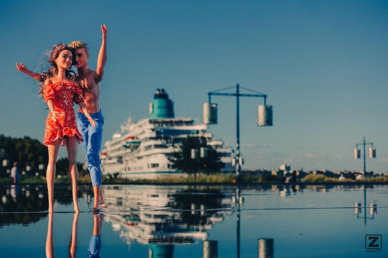 Two dolls on water with a giant (real) cruise boat in the back.