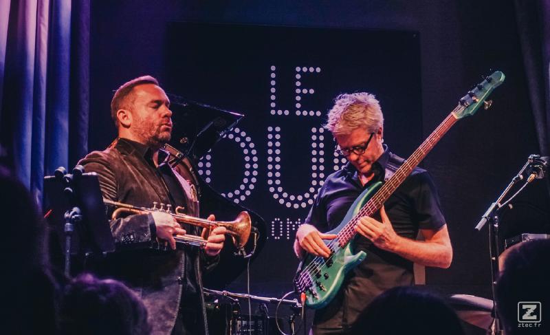 Concert photography of Kyle Eastwood playing Electric bass. he is looking at his hands and cords. Wear glasses. 
Also, there is Quentin Collins waiting to start playing Trompette eyes closed.
https://www.flickr.com/photos/ztec/53408157245/
Albums: www
