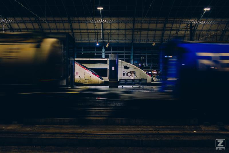 A FRET train is moving (blurred) on the foreground, leaving only two "head" of TGV on far platforms.