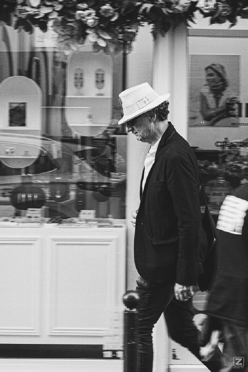 A man walking looking down. He has a white hat.