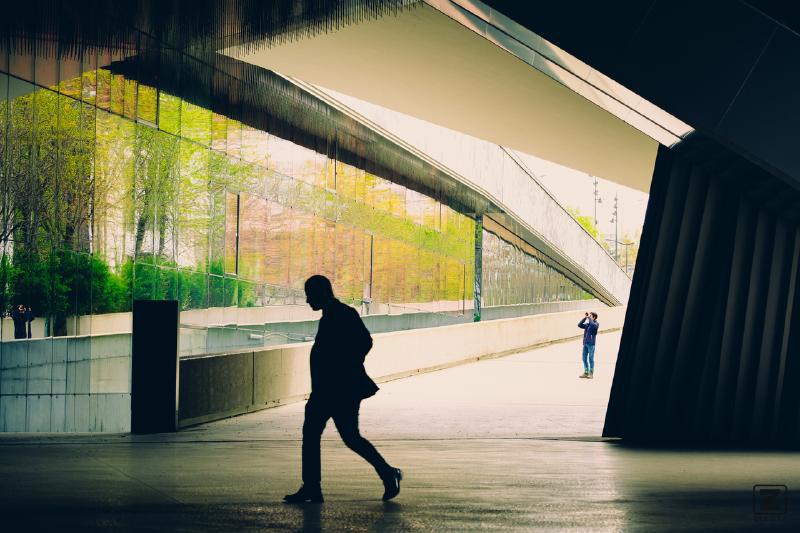 A silhouette of a man walking on the front, a photograph on the back, and a mix of light and shadow with sharp edges from the surrounding building