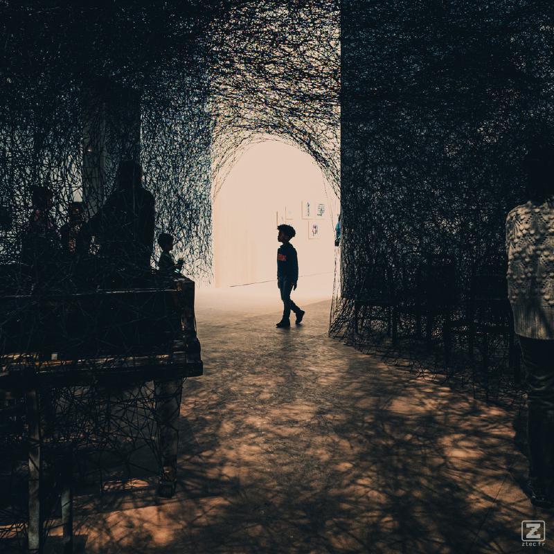 A child walking in a museum. There is black wires everywhere as part of the exposition. The child is visible as a silhouette 