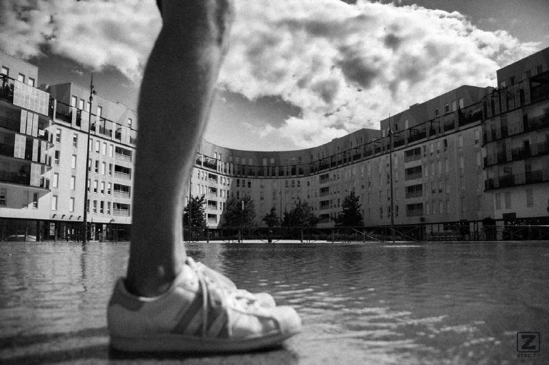 Deux pieds sur l'eau, un peu flou devant un bâtiment d'habitation moderne en U avec quelques nuages dans le ciel