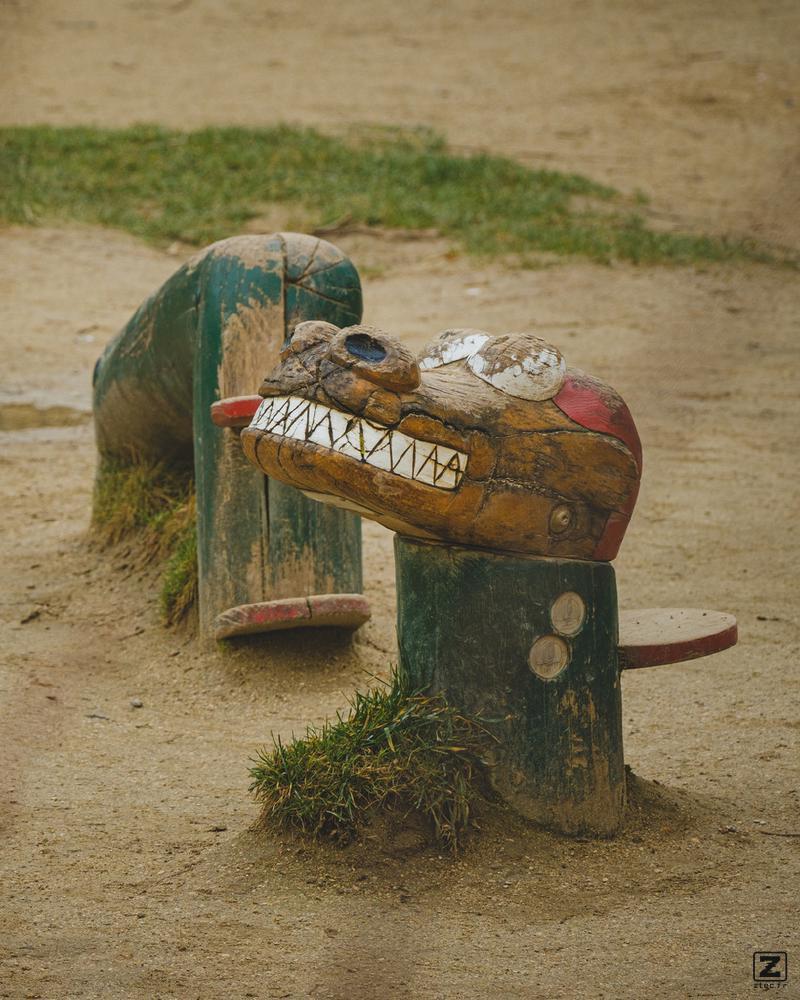 A child playground with a wooden dragon in multiple part sprouting from the ground, like the Loch Ness monster. 