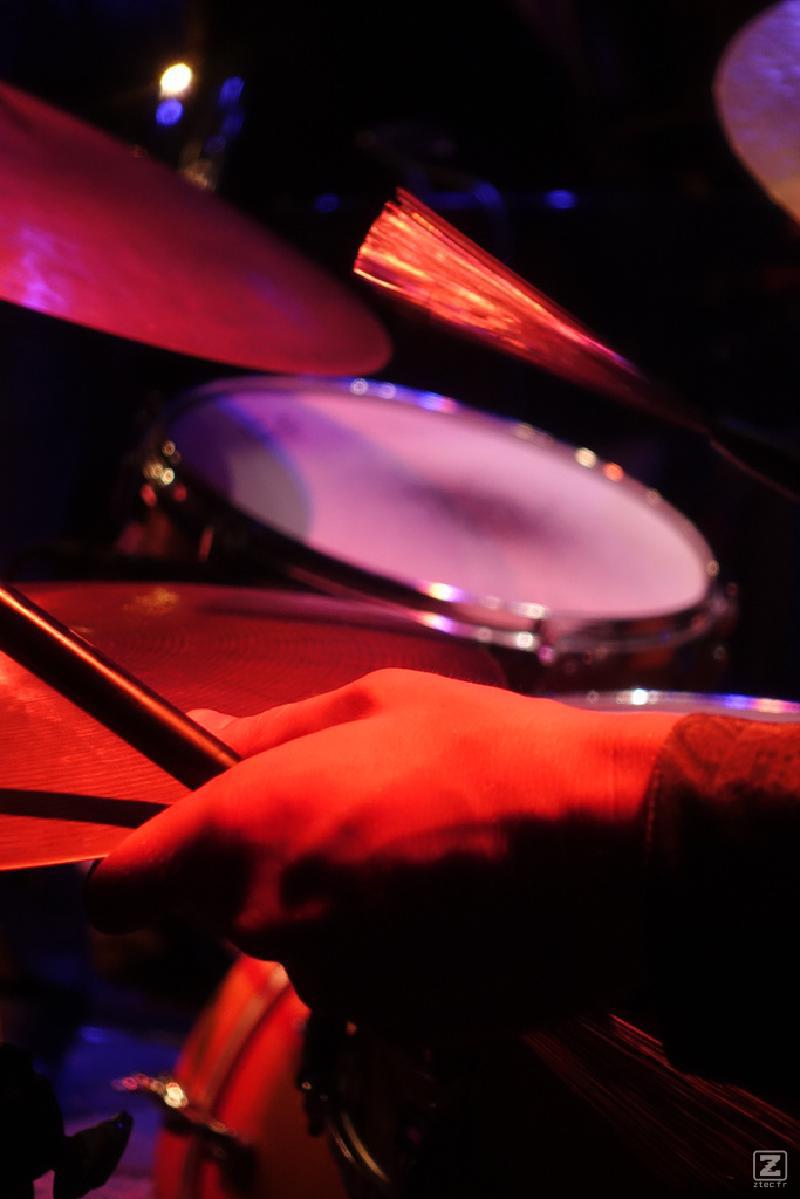 A close-up shot of a person's hand holding drumsticks over a drum set. The scene is illuminated with red and purple stage lights, creating a vibrant and dynamic atmosphere
https://www.flickr.com/photos/ztec/53891143917/