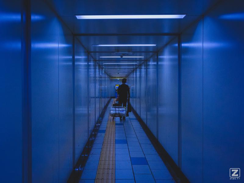 A man is pulling a chariot with a big case on it in the metro corridor. 