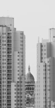 Sacré-coeur barely visible between two high rise building seen from afar. 