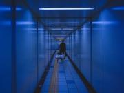 A man is pulling a chariot with a big case on it in the metro corridor. 