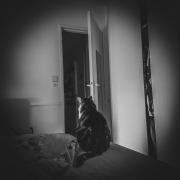 Martine is sitting on the corned of the bed, facing her back to us.