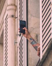 A tattooed arm out of a window taking picture with a smartphone