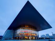 Picture of the Copenhagen opera. A bubble with glowing orange from inside (actually wood) right below a flat square that act as a roof, but go way longer outside the bubble. The picture is deforming the square making one corner pointing to the top border of the picture. Main colors are blue shared everywhere, except the bubble interior.  
    https://www.flickr.com/photos/ztec/53132985520/
