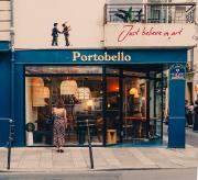 A girl is looking into the window of a store. There is design furniture in the store. The store is names "Portobello"
Right above the store, a Mosaic display two man shaking hand, one is in fire (pink Floyd cover?). Right to it, in a different style, is written "Just believe in art". 
https://www.flickr.com/photos/ztec/53159982904/