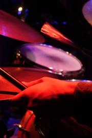 A close-up shot of a person's hand holding drumsticks over a drum set. The scene is illuminated with red and purple stage lights, creating a vibrant and dynamic atmosphere
https://www.flickr.com/photos/ztec/53891143917/