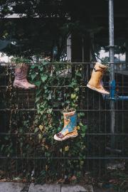 Three boots hanged on a fence as flower pots.