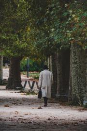 A man in a raincoat, black hat and briefcase walking in the park. Ominous