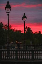 Parisian bridge with two light pole and the red sky afar.