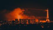 Paris from afar with the Eiffel tower. Clouds of smoke lighted in orange is visible behind buildings and the tower.