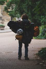A woman with a lot of equipment and bags walking in a park