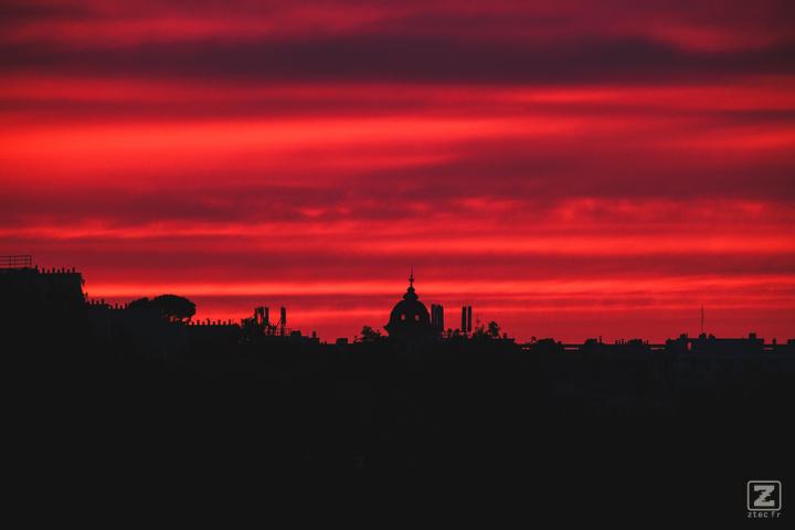 Red sky coloured by the sun rise of the morning, forming a silhouette from the roof buildings afar.