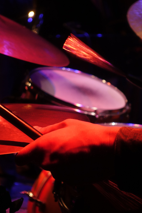 A close-up shot of a person's hand holding drumsticks over a drum set. The scene is illuminated with red and purple stage lights, creating a vibrant and dynamic atmosphere
https://www.flickr.com/photos/ztec/53891143917/