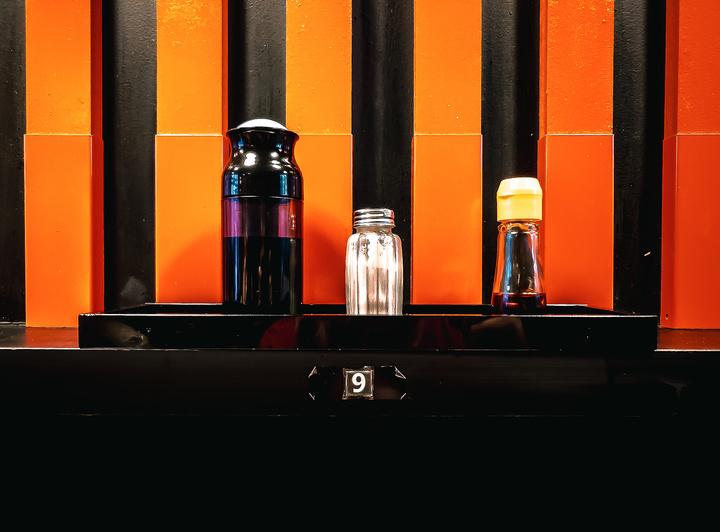 Sauces soja et condiment sur le comptoir avec le mur juste derrière composé de bandes rouge/orange et noir. Le numéro 9 est visible sur la tranche du comptoir
https://www.flickr.com/photos/ztec/53160273843/
