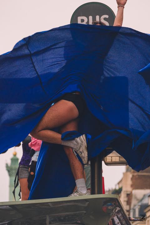 A person on top of a bus stop with a blue dress completely weighted by the wind revealing legs and feets