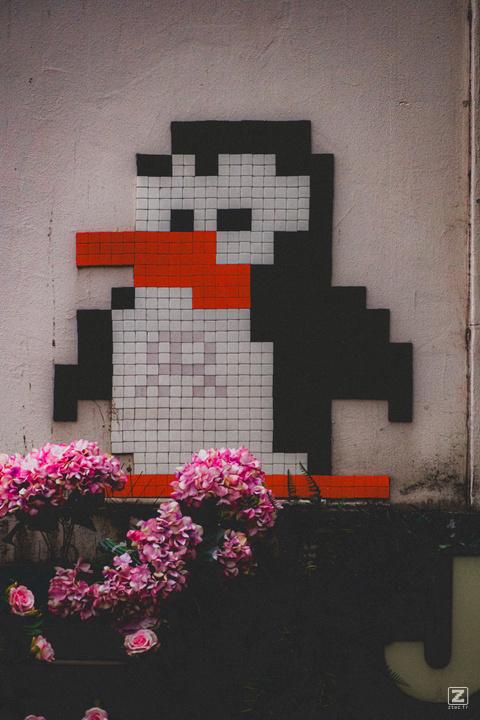 A penguin mosaic on the street. We can see a faded space invader inside the Penguin