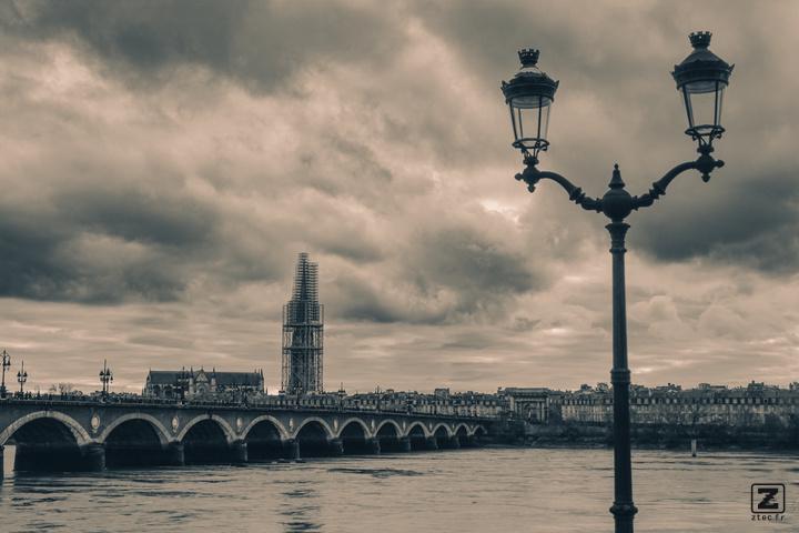 A stone bridge called Pont de Pierre crossing the Garonne in Bordeaux. You can see a twin public light on the right. On the background, you can see a tower surrounded by scaffolding for repair. 
https://www.flickr.com/photos/ztec/53412369313/
Albums: www