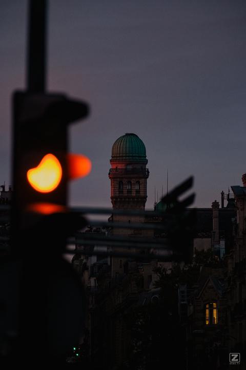 An orange traffic light, with observatory dome lighten up by the early morning sun.