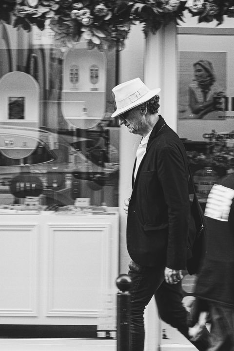 A man walking looking down. He has a white hat.