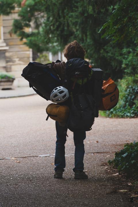 A woman with a lot of equipment and bags walking in a park