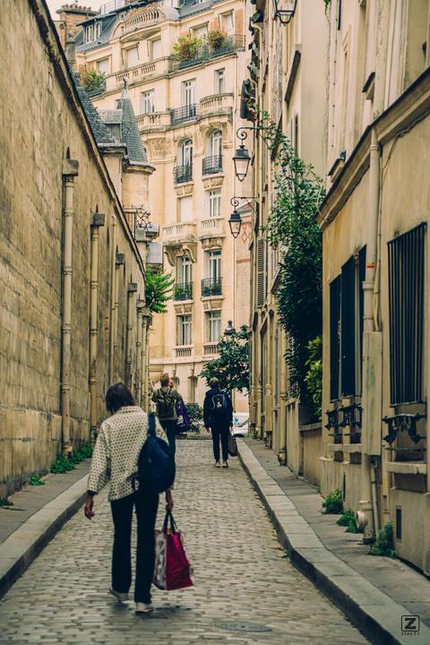 A typical small Parisian street with a woman caring groceries in a bag.