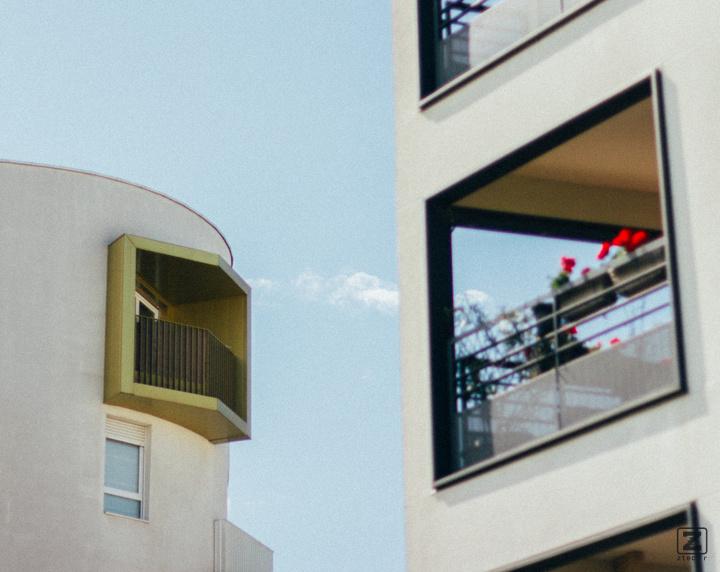 two building with two balcony. One with flower and another with a golden border. The flower one is blurry. There is grain on the picture, suggesting it is old, or is it ?
https://www.flickr.com/photos/ztec/53149082084/