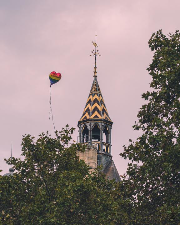 A heart shaped balloon raising in the sky in the front of a Parisian church