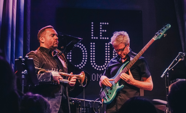 Concert photography of Kyle Eastwood playing Electric bass. he is looking at his hands and cords. Wear glasses. 
Also, there is Quentin Collins waiting to start playing Trompette eyes closed.
https://www.flickr.com/photos/ztec/53408157245/
Albums: www