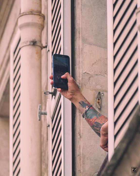 A tattooed arm out of a window taking picture with a smartphone