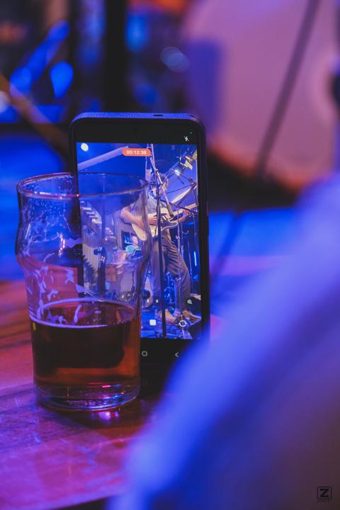 A phone left against a beer glass to record the concert. Jean-Loup is playing guitar is visible on the screen