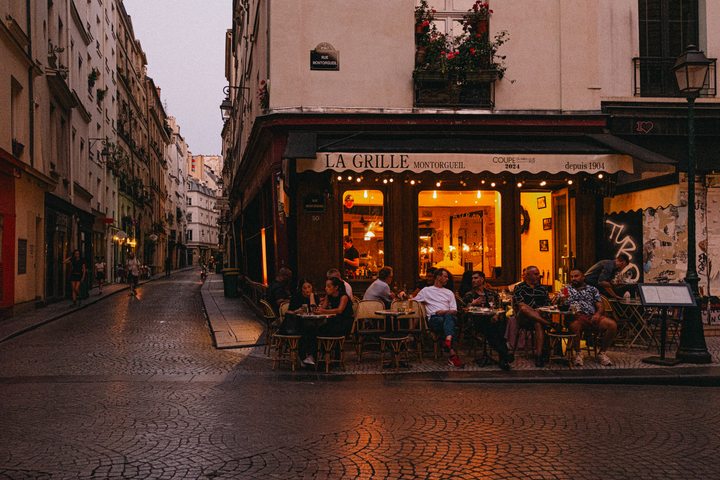 A bar in Paris (rue Montorgueil) with warm light coming from inside, reflecting on the pavement. 