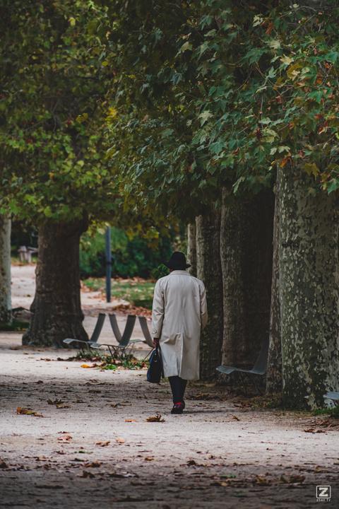 A man in a raincoat, black hat and briefcase walking in the park. Ominous