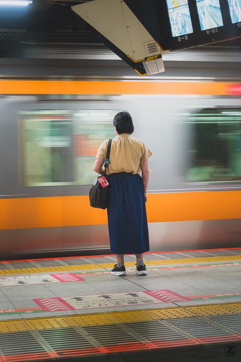 A woman is waiting for her train on the platform. One is moving. blurred by it's movement of going away.
