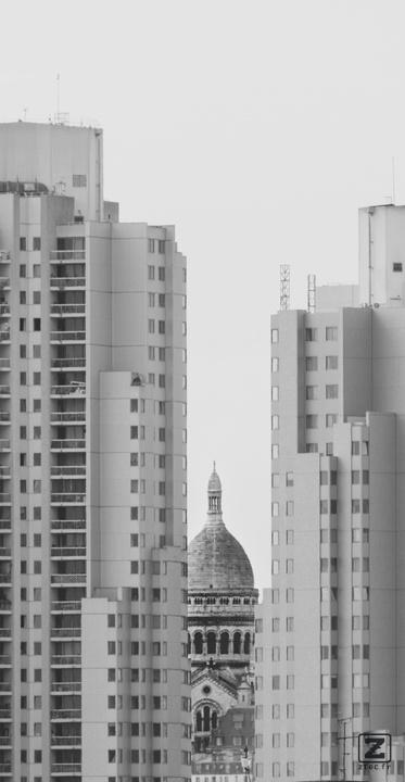 Sacré-coeur barely visible between two high rise building seen from afar. 