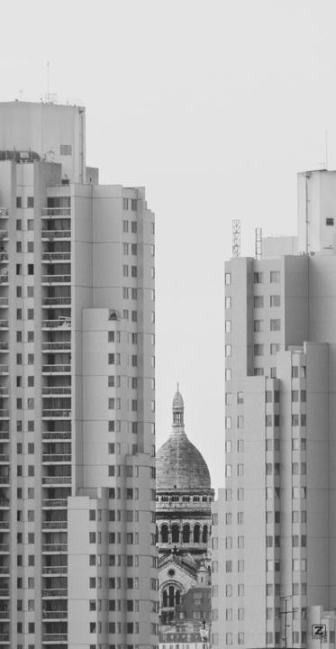 Sacré-coeur barely visible between two high rise building seen from afar.