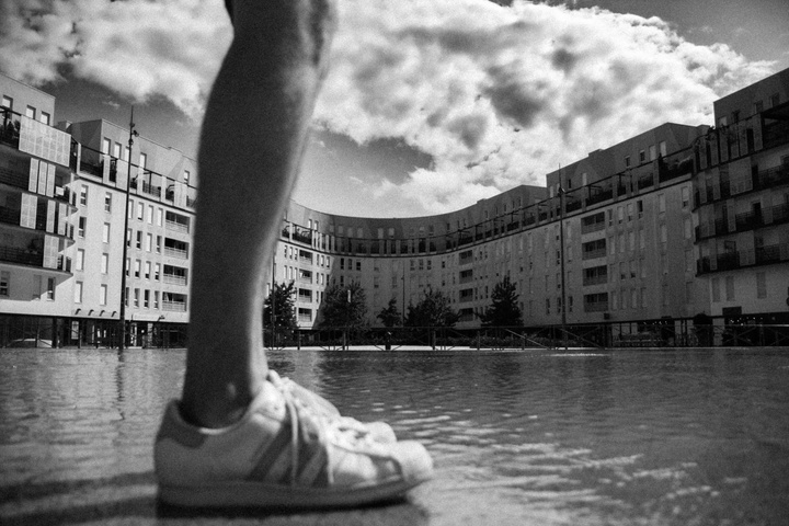Deux pieds sur l'eau, un peu flou devant un bâtiment d'habitation moderne en U avec quelques nuages dans le ciel