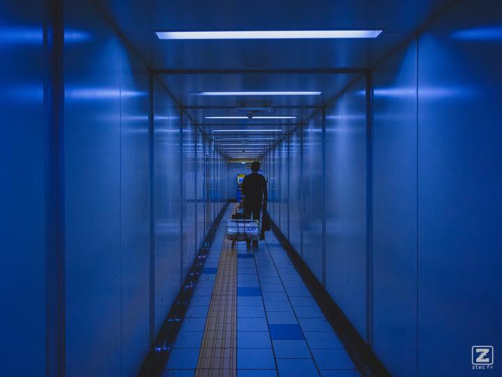 A man is pulling a chariot with a big case on it in the metro corridor. 