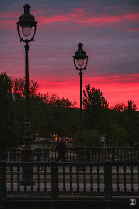 Parisian bridge with two light pole and the red sky afar.