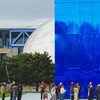 A blue building in front of a mirror sphere, with people waiting in line in front.