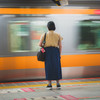 A woman is waiting for her train on the platform. One is moving. blurred by it's movement of going away.