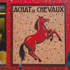 A tilled wall with a drawing of a horse and the title "Achat de Chevaux". Someone is standing on the right, not really happy. 
