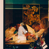 A peek inside a restaurant though a window, with a lady in the glass reflection.